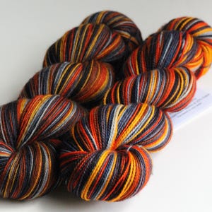 May include: A collection of colorful yarn skeins. The yarn features a striped pattern with shades of orange, yellow, black, and gray. The yarn is arranged on a white surface, showcasing the vibrant colors and textures.