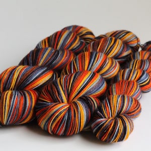 May include: A collection of colorful yarn skeins. The yarn is a mix of orange, yellow, blue, and black, creating a striped effect. The skeins are arranged in a cluster, suggesting a craft or knitting project.