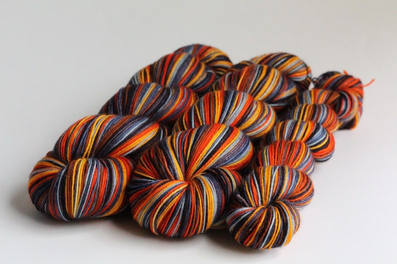 May include: A collection of colorful yarn skeins. The yarn is a mix of orange, yellow, blue, and black, creating a striped effect. The skeins are arranged in a cluster, suggesting a craft or knitting project.