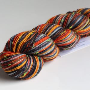 May include: A skein of colorful yarn with orange, yellow, gray, and navy blue strands. The yarn has a speckled appearance with small flecks of green. The yarn is likely used for knitting or crocheting projects.
