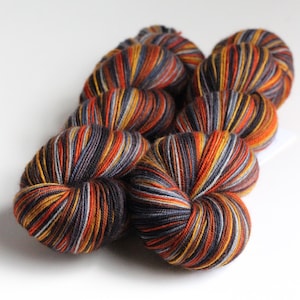 May include: Several skeins of yarn in a variety of colors, including orange, yellow, gray, and black. The yarn is arranged in a cluster, with the individual skeins visible. The yarn is likely for knitting or crocheting projects.