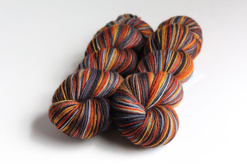 May include: Several skeins of yarn in a variety of colors, including orange, yellow, gray, and black. The yarn is arranged in a cluster, with the individual skeins visible. The yarn is likely for knitting or crocheting projects.