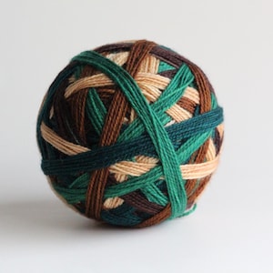 May include: A ball of yarn with a woven pattern of green, brown, and tan threads. The yarn is tightly wound, creating a spherical shape. The yarn ball is suitable for knitting and crochet projects.
