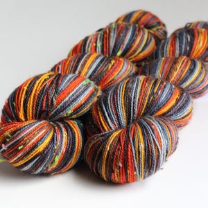 May include: A collection of colorful yarn skeins. The yarn features a mix of orange, yellow, gray, and black strands, creating a textured appearance. The skeins are arranged in a cluster, showcasing the vibrant color palette and potential for crafting projects.