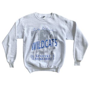 May include: Gray sweatshirt with a blue and white graphic print of basketball players. The graphic says "Rim Rockin' Wildcats Kentucky Basketball".