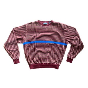 May include: A long-sleeved striped sweater with a blue stripe across the chest. The sweater is maroon and white.