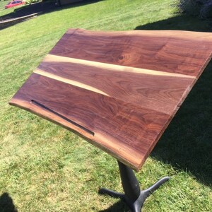 May include: A large, dark brown wooden table top with a live edge and a black metal groove. The table top is made of walnut wood and has a natural, rustic finish.