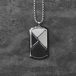 Pode incluir: Um pingente de placa de identificação prateado com um design geométrico. O pingente apresenta seções pretas, brancas e prateadas, suspensas por uma corrente combinando. O texto "JUNIPER & ELOISE JEWELRY" é exibido no canto superior direito.