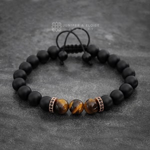 Op de afbeelding: Zwarte matte kralen armband met twee tijgeroog kralen met accenten van roségoud en zwarte diamanten. Juniper & Eloise Jewelry.