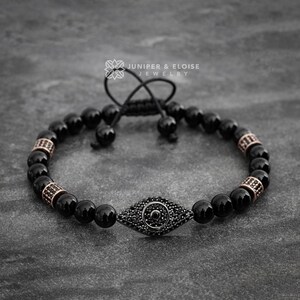 Può includere: Braccialetto con perline di onice nero con un ciondolo di occhio turco nero con un centro di cristallo nero. Il braccialetto ha una chiusura a cordoncino nero con un fermo argentato.