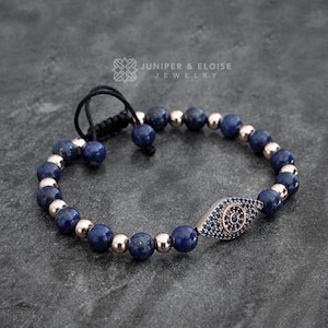 Op de afbeelding: Een blauwe lapis lazuli kralen armband met een roségouden boze oog bedel. De armband heeft een zwarte koordsluiting. Juniper & Eloise Jewelry.