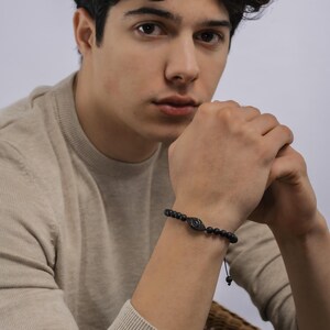 May include: A black beaded bracelet with a black evil eye charm. The bracelet is adjustable with a black cord.