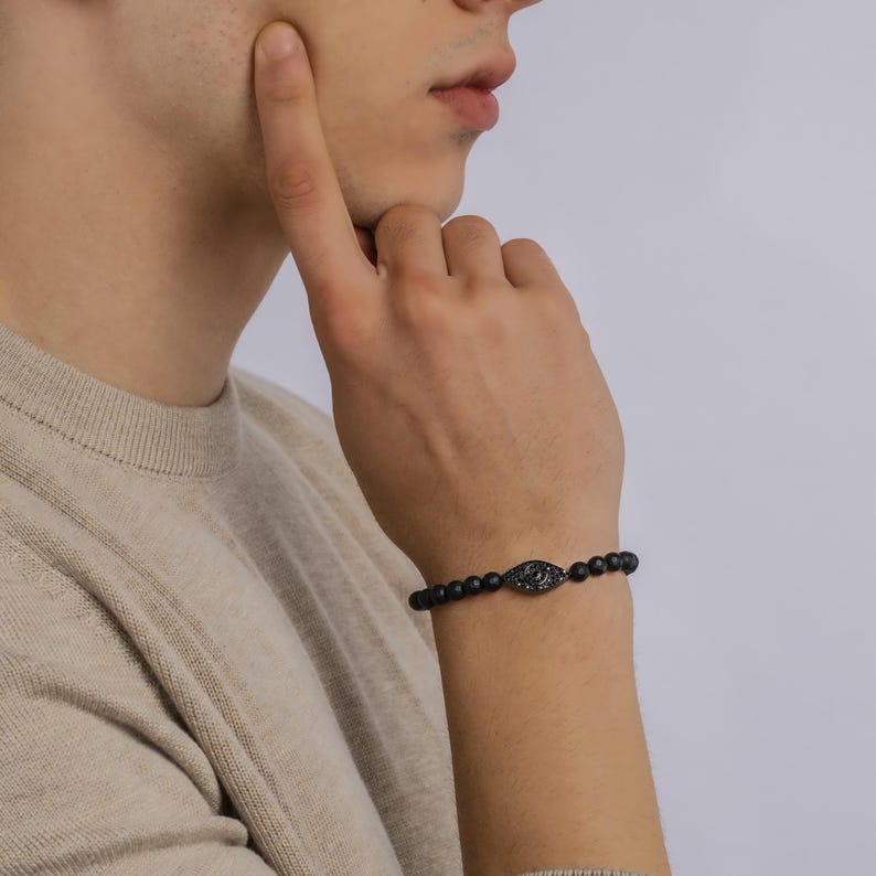 May include: A black beaded bracelet with a black evil eye charm. The charm is set with small black stones.