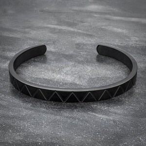 May include: A black metal bracelet with a geometric pattern. The bracelet is made of a smooth, polished metal and has a simple, modern design.