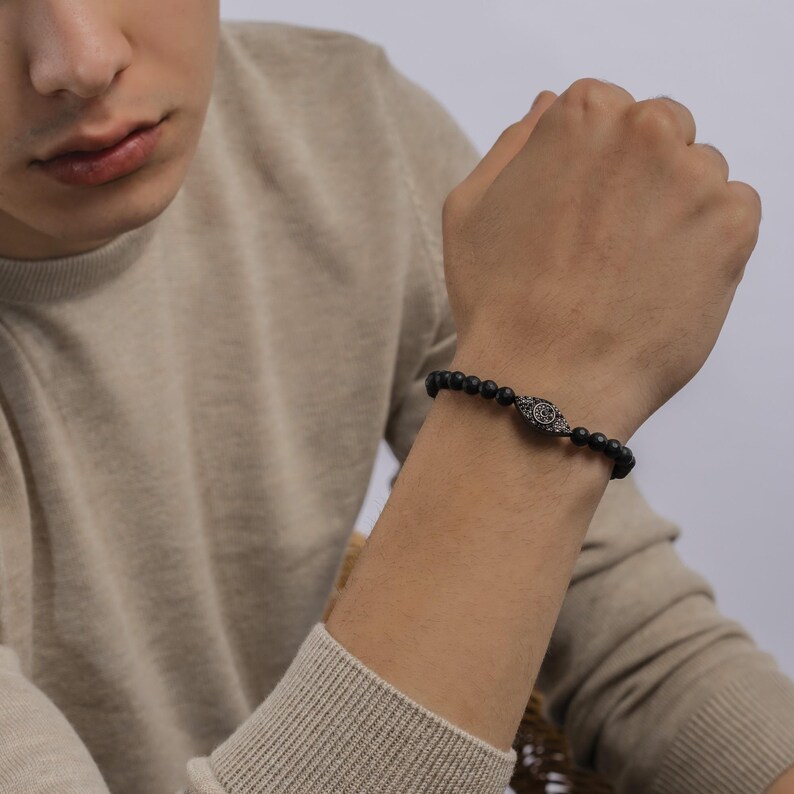 May include: A black beaded bracelet with a silver eye charm. The eye charm is adorned with small, clear rhinestones.