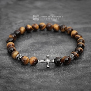 May include: A brown tiger's eye beaded bracelet with a silver cross charm. The bracelet is made with natural stones and has a simple design.