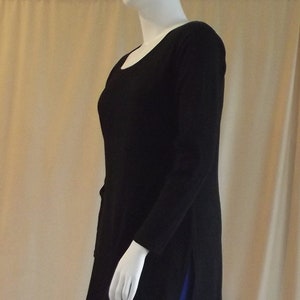 May include: A black long-sleeved tunic and royal blue leggings are shown from the side. The tunic has a scoop neck and side slits. The leggings are a solid blue. The image text reads: "Side view of size 16 long sleeve black tunic, worn with royal blue long leggings."