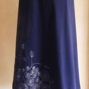 Könnte beinhalten: Ein dunkelblaues, kurzärmeliges, knielanges Kleid mit einem weißen Blumendesign am Saum.