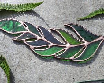May include: A stained glass leaf with a copper wire hanger. The leaf is made of green and black glass and has a detailed design.