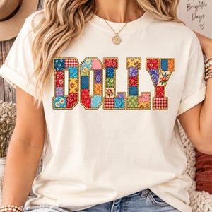 Könnte beinhalten: Ein cremefarbenes Kurzarm-T-Shirt mit dem Wort DOLLY in großen Blockbuchstaben. Jeder Buchstabe ist mit einem bunten Patchwork-Muster gefüllt, das aus verschiedenen Blumen-, Vichy- und Paisley-Drucken in Rot, Blau und Gelb besteht.