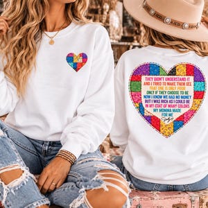 May include: A white long-sleeve sweatshirt featuring a small multicolored patchwork heart on the front left chest and a large matching patchwork heart on the back containing the text: THEY DIDN'T UNDERSTAND IT AND I TRIED TO MAKE THEM SEE THAT ONE IS ONLY POOR ONLY IF THEY CHOOSE TO BE NOW I KNOW WE HAD NO MONEY BUT I WAS RICH AS I COULD BE IN MY COAT OF MANY COLORS MY MOMMA MADE FOR ME.