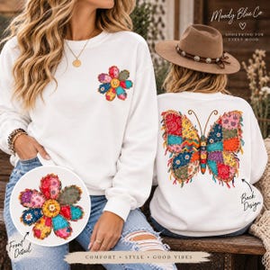 May include: A white long-sleeve sweatshirt featuring a colorful patchwork-style flower graphic on the front left chest and a large, vibrant patchwork butterfly design on the back. The fabric displays intricate, multi-colored floral and geometric patterns.