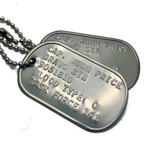May include: Two silver dog tags with a chain. The top tag reads "CAP. JOHN PRICE NO SIX". The bottom tag reads "CAP. JOHN PRICE BRAVO SIX 9051210 BLOOD TYPE: O TASK FORCE 141".