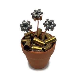 May include: A terracotta flower pot filled with spent bullet casings. Three bullet casings are arranged as flowers with copper stems.