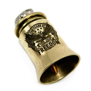 May include: A brass-colored bell crafted from a spent bullet casing, featuring an engraved eagle emblem with the text 250 YEARS OF FREEDOM and 1776-2026. A small copper-toned bullet tip hangs inside the bell, and a silver-toned metal ring is attached.