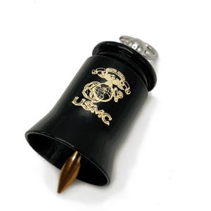 May include: Black bell-shaped object with a gold USMC emblem and the words "Semper Fidelis". A silver ring is attached to the top. The bell has a bronze-colored tip.