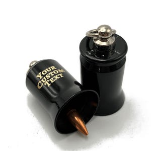 May include: Black bullet-shaped bottle stoppers with a copper-colored tip. One stopper is lying on its side, displaying the text "YOUR CUSTOM TEXT" in gold lettering. The other stopper is upright, with a silver ring and ball on top.