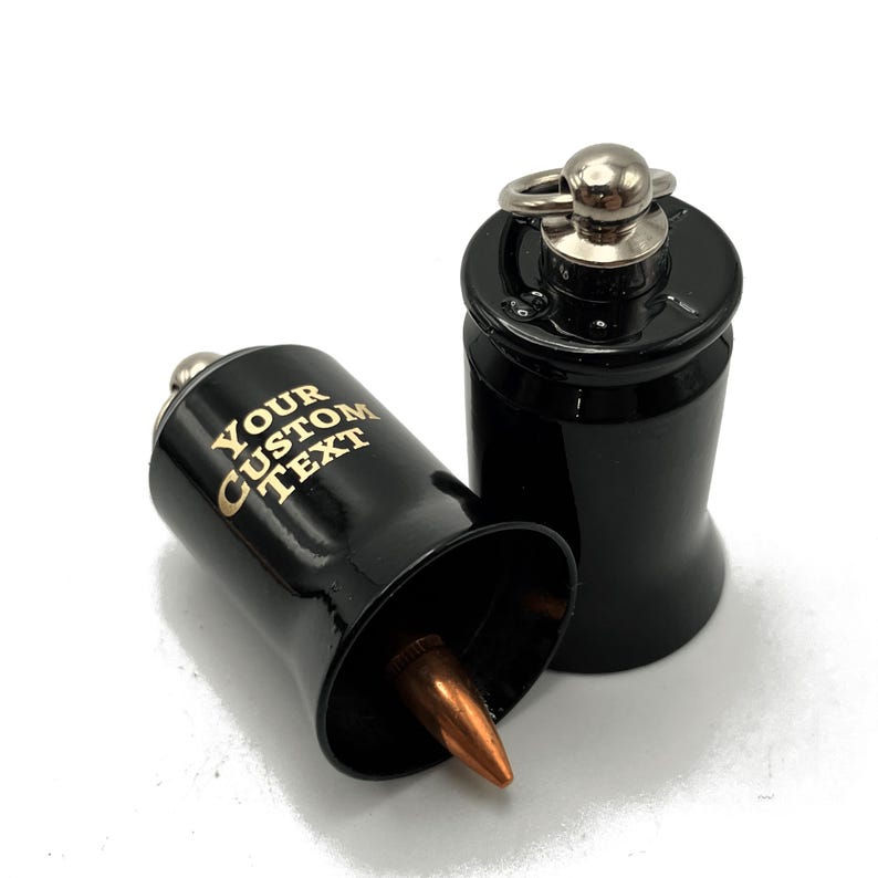 May include: Black bullet-shaped bottle stoppers with a copper-colored tip. One stopper is lying on its side, displaying the text "YOUR CUSTOM TEXT" in gold lettering. The other stopper is upright, with a silver ring and ball on top.