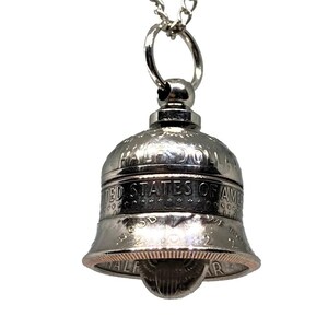 May include: A silver bell pendant necklace made from a half dollar coin. The coin is engraved with "Half Dollar", "United States of America", and "In God We Trust".