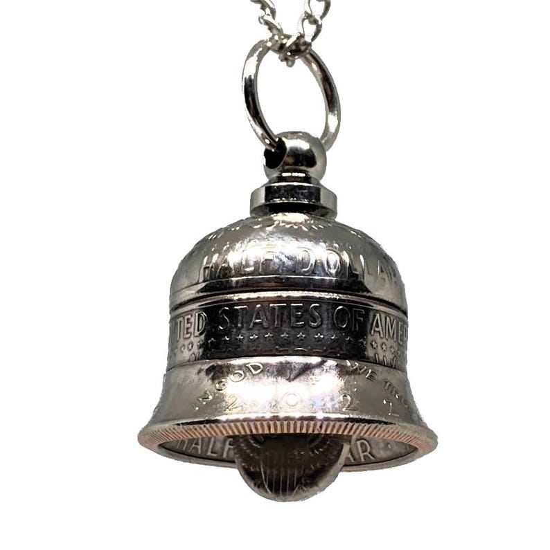 May include: A silver bell pendant necklace made from a half dollar coin. The coin is engraved with "Half Dollar", "United States of America", and "In God We Trust".