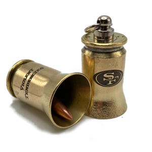 May include: Two gold-colored bullet casings, one with the text "VIOLENT TENDENCIES" engraved on the side and the other with the San Francisco 49ers logo engraved on the side.