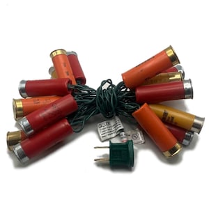 May include: A string of Christmas lights with red, orange, and yellow shotgun shell-shaped bulbs. The lights are strung on a green wire and have a standard plug.