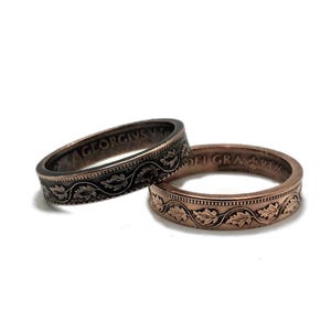 May include: Two rings made from old coins. One ring is copper with a design of leaves and the other ring is black with a design of leaves. The text "GEORGIVS V DEI GRA" is visible on the black ring.