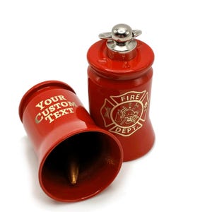 May include: Two red metal bells. One bell has the text "YOUR CUSTOM TEXT" in gold lettering. The other bell has a gold emblem that says "FIRE DEPT". The bells have a silver handle on top.