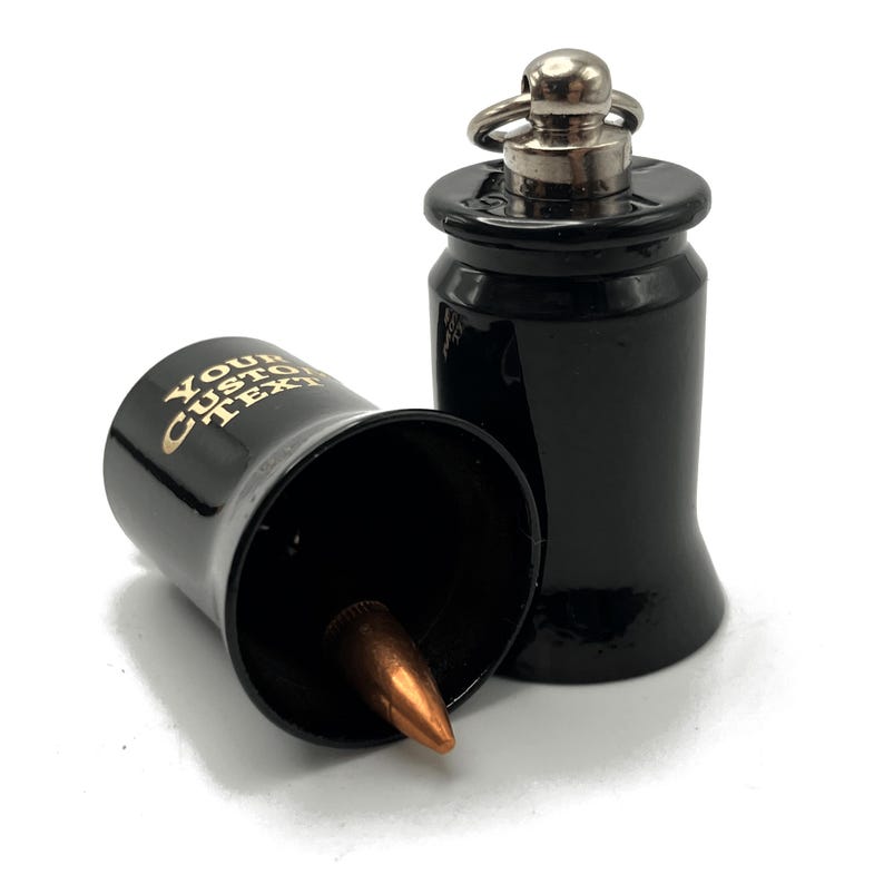 May include: Two black bullet-shaped bottle stoppers. One is upright, the other is on its side, revealing a copper-colored bullet. The side of the stopper has the text "YOUR CUSTOM TEXT" in gold lettering. The stoppers have a silver-colored ring and top.
