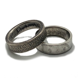 May include: Two silver-toned coin rings crafted from United States half dollar coins. One ring displays the text UNITED STATES OF AMERICA, while the other shows the year 1964, the words HALF DOLLAR, and the phrase IN GOD WE TRUST.