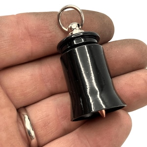 May include: A black, glossy, bell-shaped keychain pendant with a silver ring and a copper-colored tip. The pendant has a cylindrical top and a flared bottom. The keychain is held in a hand.