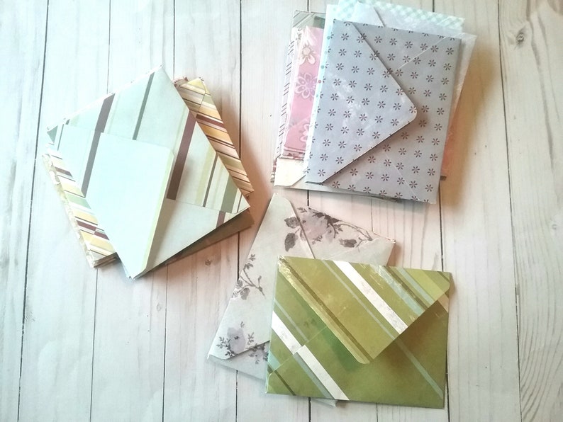 May include: A stack of patterned envelopes in various colors, including green, brown, pink, and gray. The envelopes have different designs, including stripes, floral patterns, and polka dots.