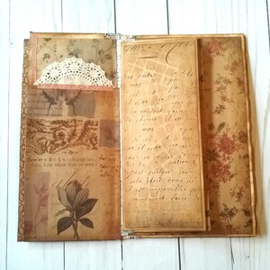 May include: An open journal with pages decorated with vintage floral patterns and handwritten text. The journal has a lace embellishment on the front cover.