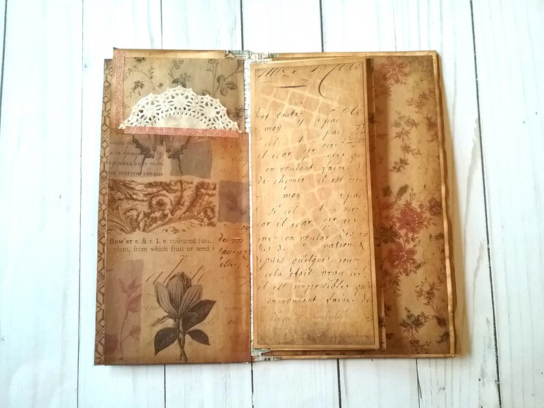 May include: An open journal with pages decorated with vintage floral patterns and handwritten text. The journal has a lace embellishment on the front cover.