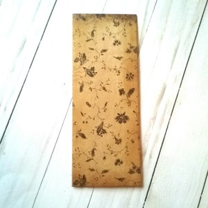 May include: A brown paper envelope with a floral pattern printed on it. The envelope is lying flat on a white wooden surface.