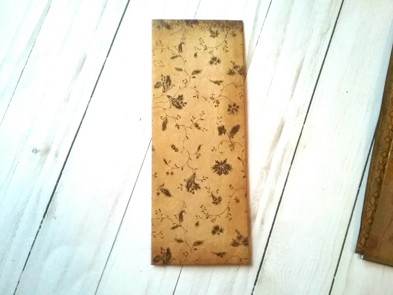 May include: A brown paper envelope with a floral pattern printed on it. The envelope is lying flat on a white wooden surface.