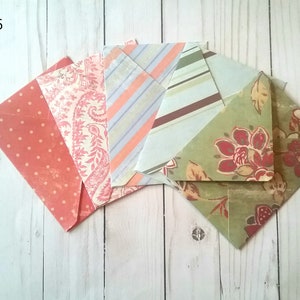 May include: Pack of six decorative envelopes with various patterns. The envelopes are in shades of pink, green, and brown with floral and geometric designs. The text "Pack 6" is visible in the top left corner of the image.