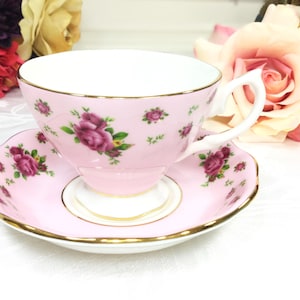 May include: A pink teacup and saucer set with a floral rose pattern. The teacup and saucer are trimmed with gold and feature a delicate design of burgundy roses and green leaves. The set is designed for tea parties.