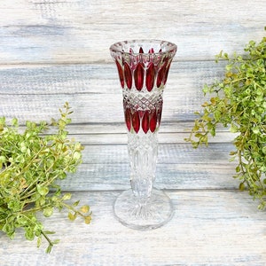 May include: A clear glass vase with a red interior design. The vase has a flared top and a long, slender stem. The base is round and clear. The vase is likely used for displaying flowers and other decorative items.