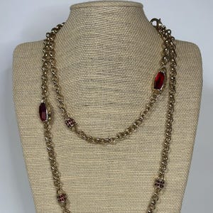May include: A gold chain necklace with red gemstone accents. The necklace is layered and features rectangular red stones.